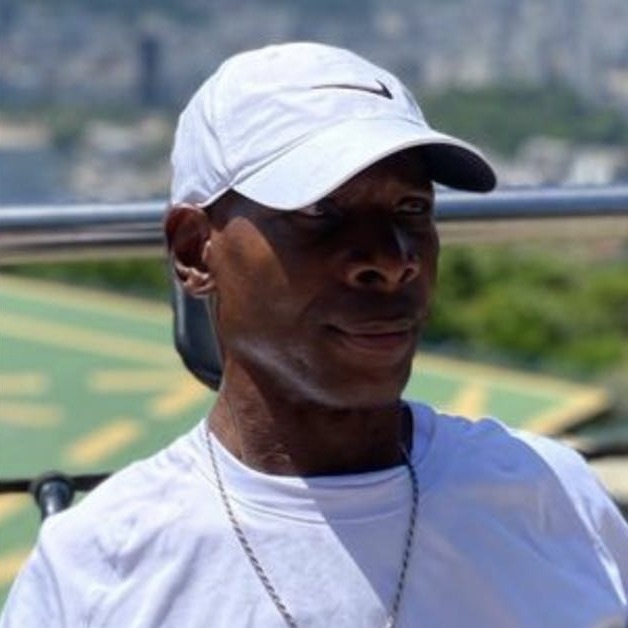 John E. Mason smiling outdoors in a white cap and white T-shirt