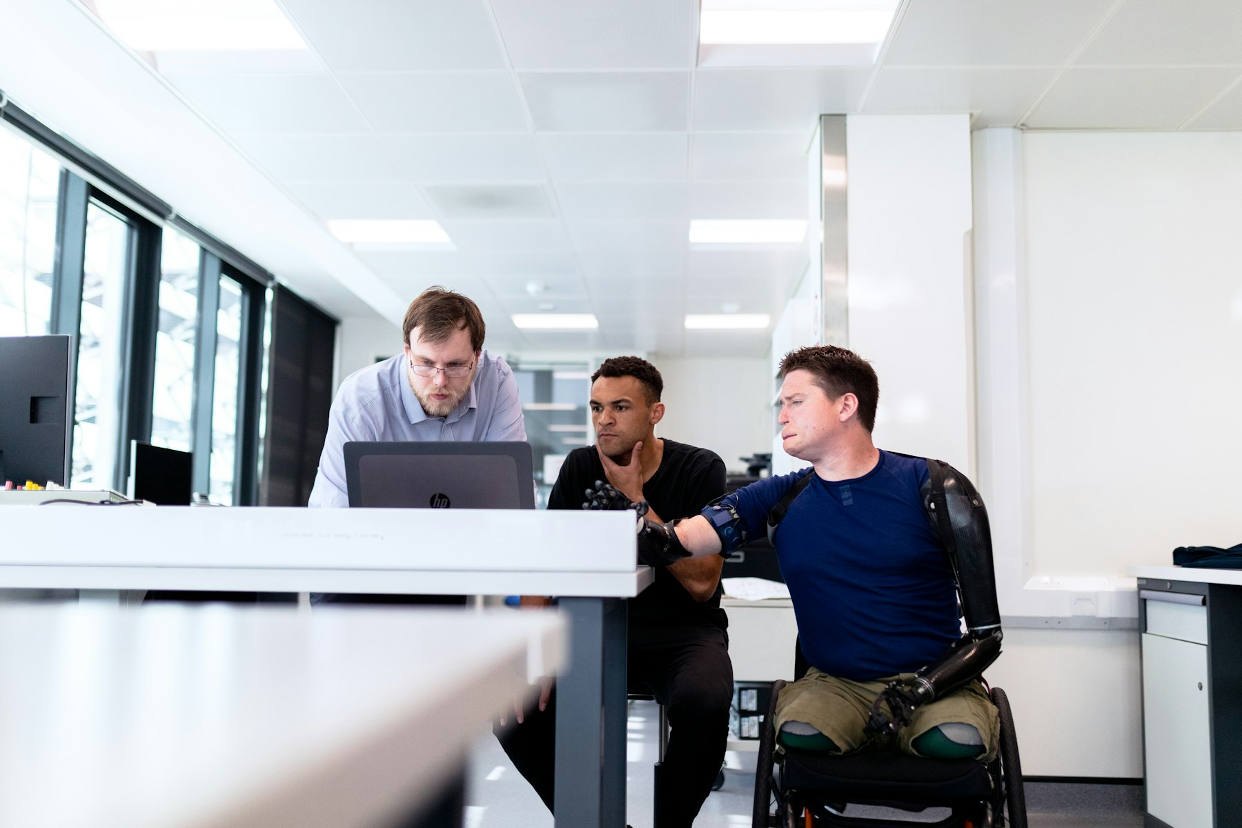 Colleagues collaborating at an office desk, one working from a wheelchair